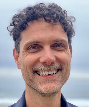 Headshot of Andrew with a coastal sky backdrop.