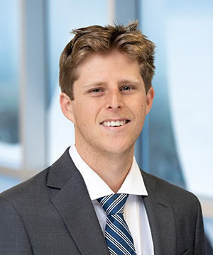 Professional headshot of Avery in a grey suit.