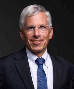 A professional headshot of Board member Bill Jeffrey in a black suit in front of a black background.