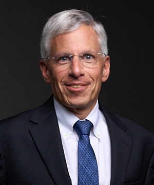 A professional headshot of Board member Bill Jeffrey in a black suit in front of a black background.