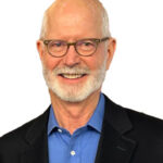 A headshot of Bruce in a black blazer and blue collared shirt.