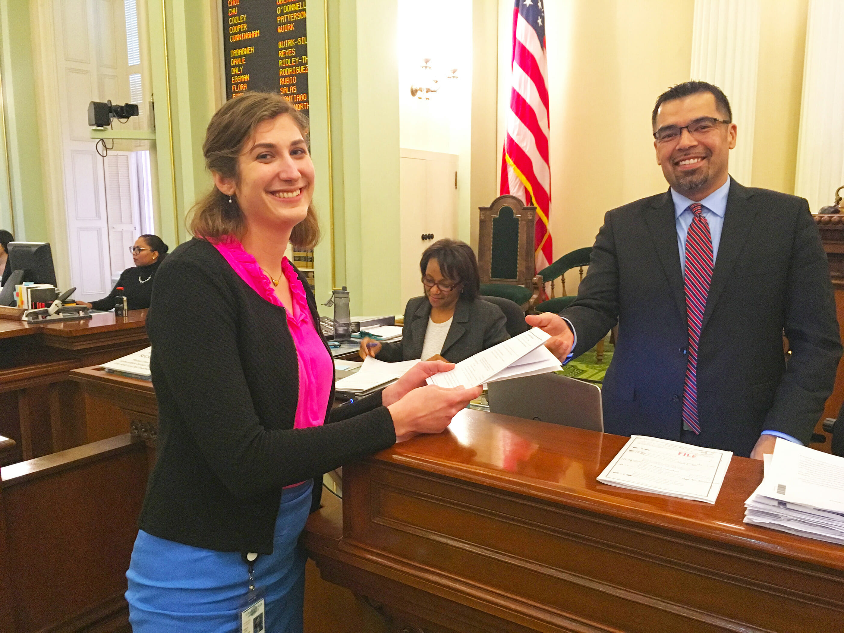 Photo of Jen Chase, PhD, a 2017 CCST Science & Technology Policy Fellow, handing a bill across the desk on the floor of the California State Assembly.