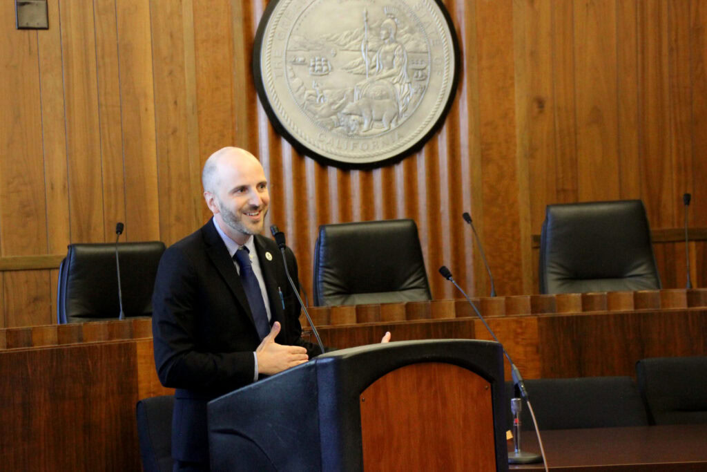 CCST Director of Strategic Initiatives Mikel Shybut, PhD, speaking into a microphone in the Legislative Office Building.