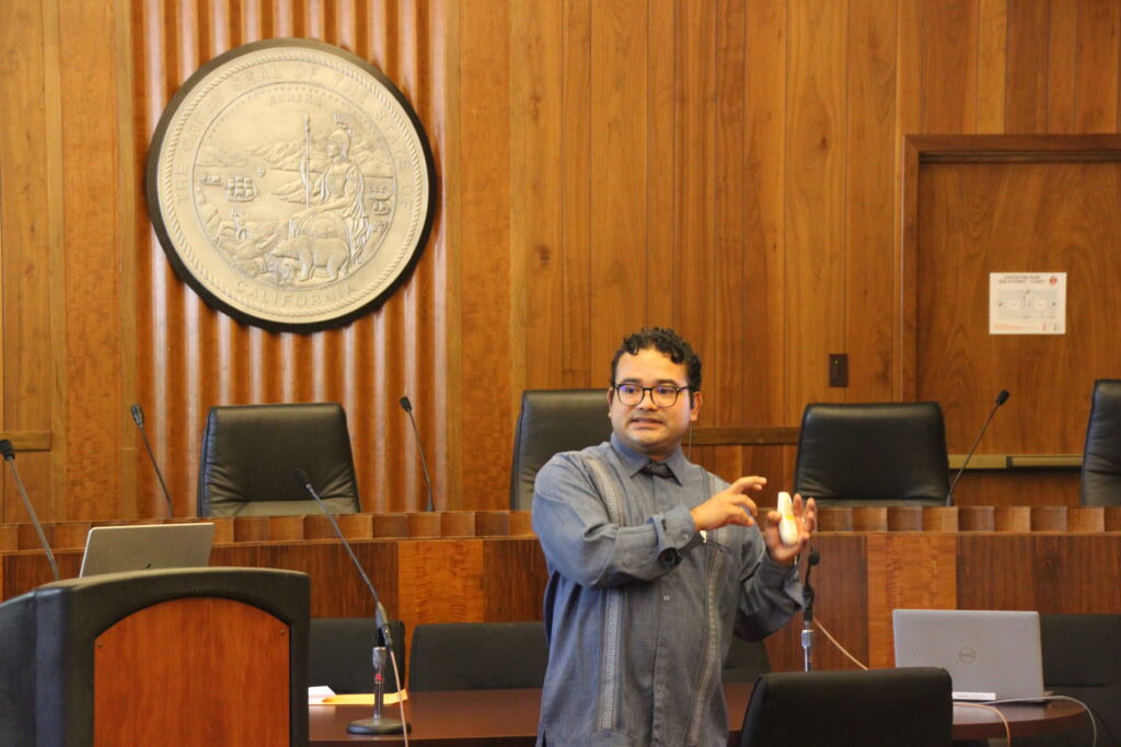 CCST Senior Science Officer Héctor Corzo, PhD, speaks at the front of the room in a Legislative Office Building.