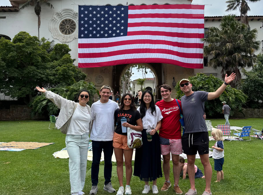 Photo of Fernando with five friends in front of an American flag hanging in Santa Barbara. 
