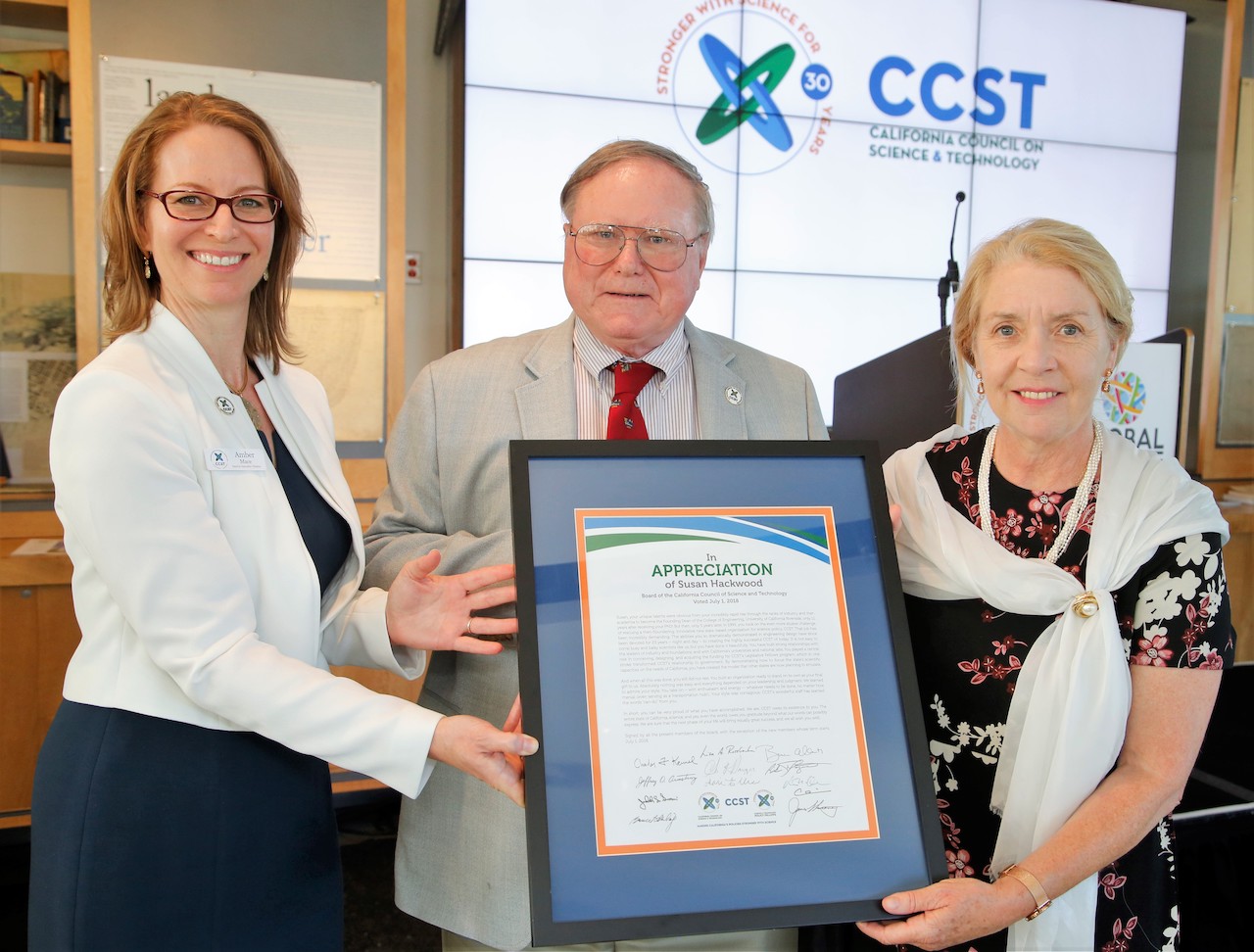 Three people holding a framed letter of appreciation in front of a screen projected with CCST's logo.