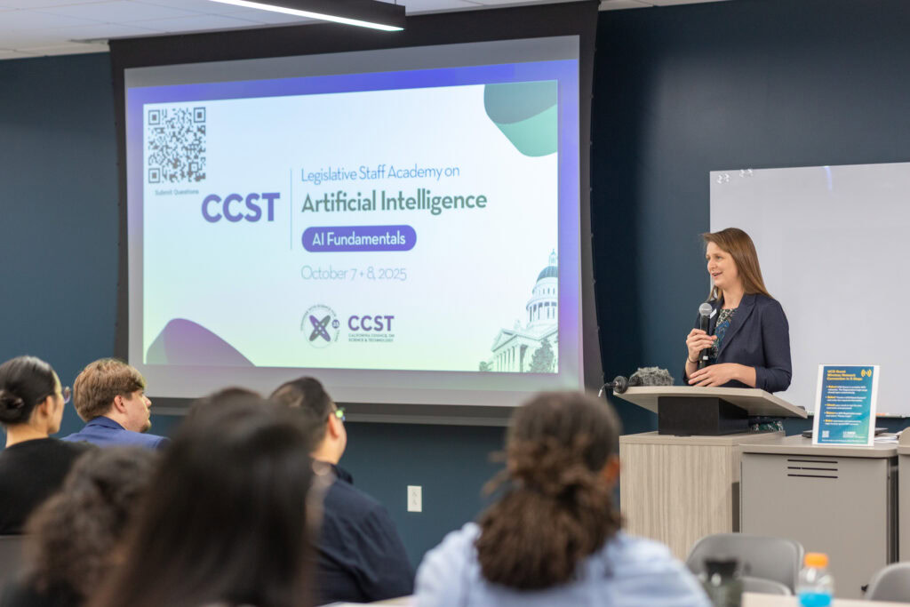 CCST CEO Julianne McCall, PhD, speaking into a microphone in front of a projector screen.