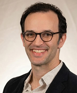 Headshot in a button down and suit jacket in front of a cream background.