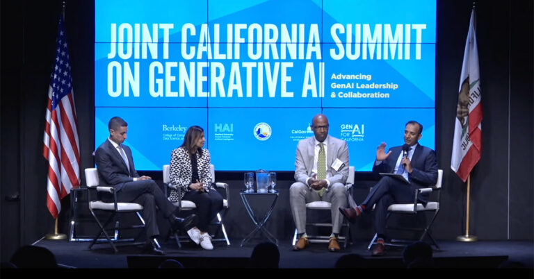 A photo of four panelists sitting on a stage with a large screen behind them showing the title, "Joint California Summit on Generative AI," with the US and California flags on the left and right of the stage.
