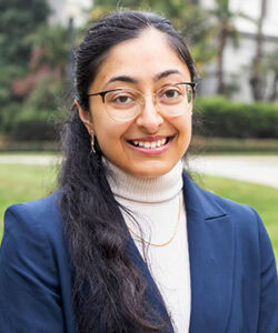 Professional headshot of Manisha in a blazer and turtleneck in front of the California State Capitol Building.