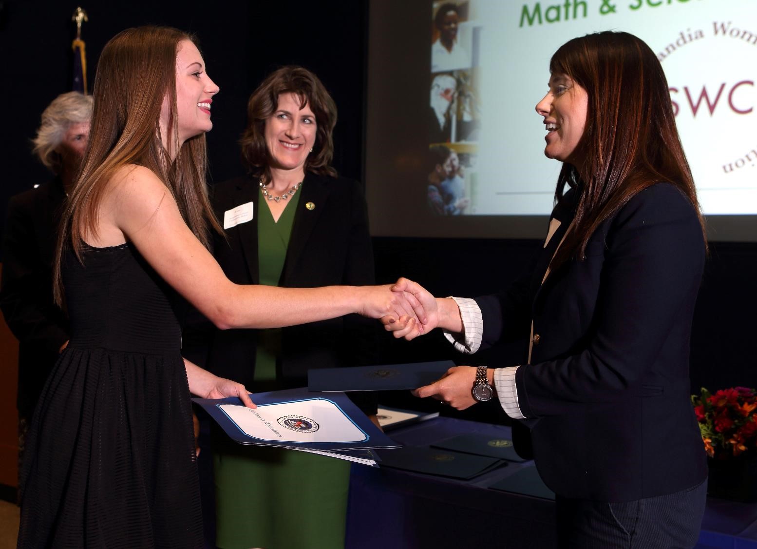 An award recipient shakes hands with the person granting them the award on stage.