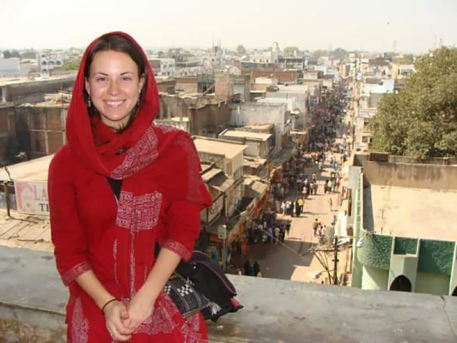 Laura McWilliams is leaning against a concrete railing, which overlooks a busy city street in India, full of people and stalls.