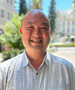 A profile photo of Perry standing in front of the California State Capitol area.