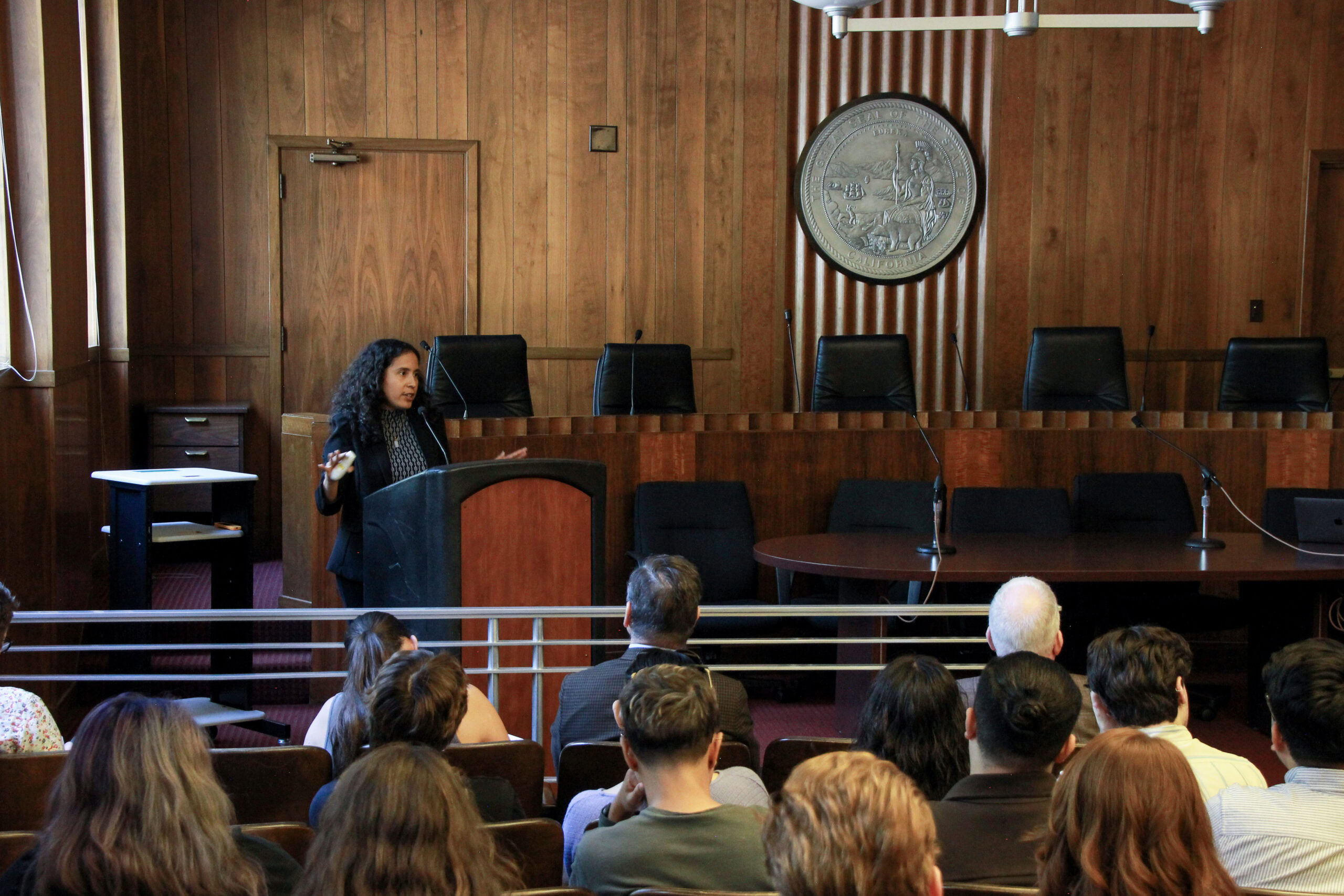 Tanny Chavez Esparza, Computational Research Scientist at Lawrence Berkeley National Laboratory, speaks to an audience of legislative staff at a podium in a room in the Legislative Building of the California State Capitol.